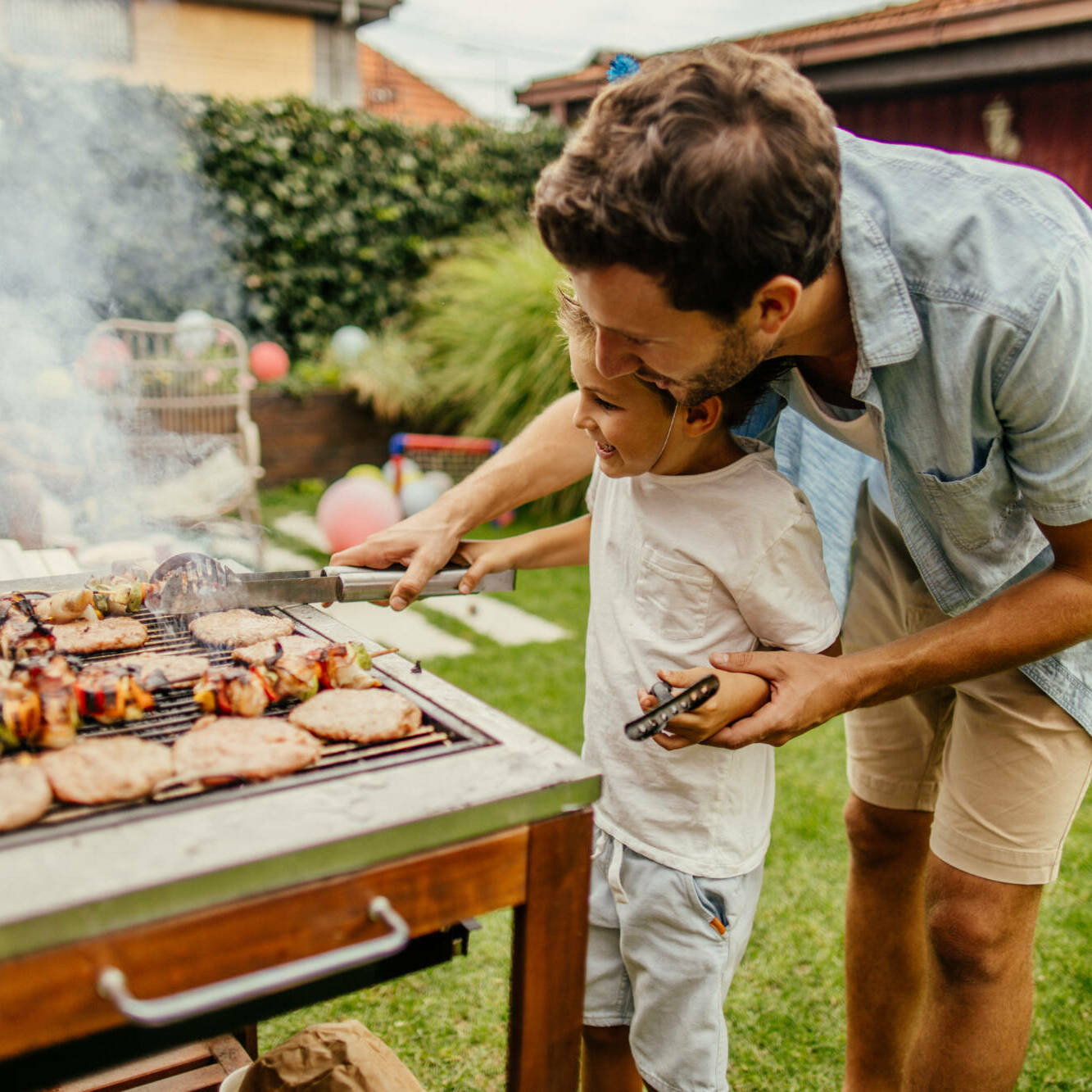 Photo of father and son grilling meat during the barbecue party in their yard