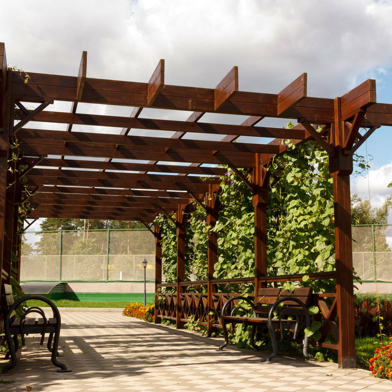 Wooden pergollas from natural wood with comfortable benches in a modern country village on a sunny summer day. The paved path is laid past flower beds, ornamental shrubs and trees. Russia. Close-up